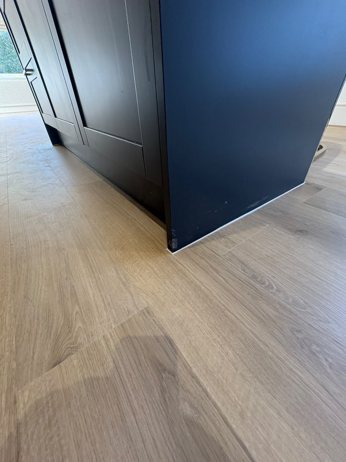Light oak wood flooring shown in a room setting, with a dark blue cabinet or panel standing in the upper left corner.