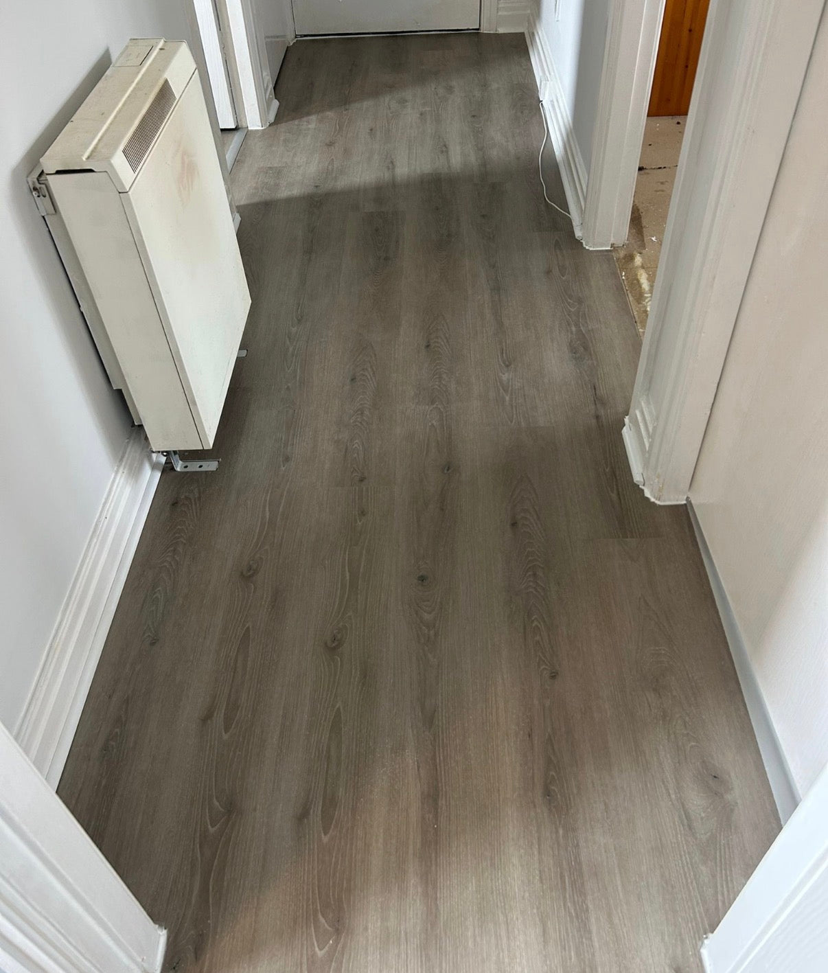 Gray wood-look laminate flooring installed in a residential hallway with white walls and baseboards.