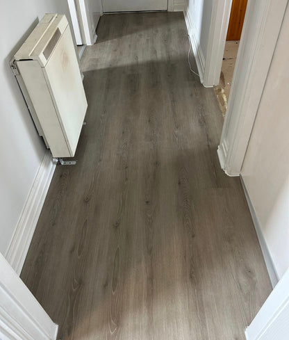 Gray wood-look laminate flooring installed in a residential hallway with white walls and baseboards.